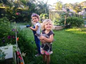 Young children watering vegetable garden and cuddling chicken