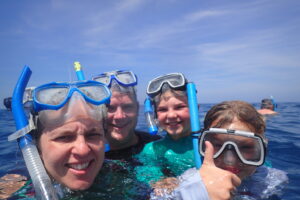 Mother, Father and two young daughters in crystal clear blue water with snorkels on their faces to go and explore the reef off Mana Island Fiji.