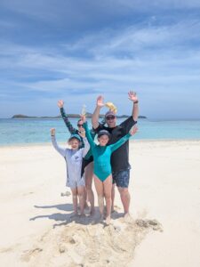 Family of four standing on Mana Island Sandbar white sand with crystal clear blue water and island in the background